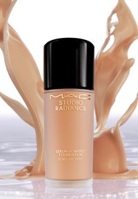 MAC Studio Radiance serum-gebaseerde foundation in een heldere glazen fles, met een zwarte dop, bevat een licht bruine vloeistof en gouden tekst.