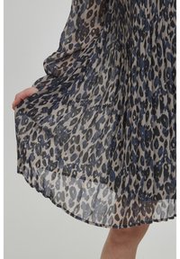 Plisserad klänning i lätt, genomskinlig tyg med leopardmönster i nyanser av blått, svart och beige. Betonade detaljeringar vid nederkanten synliga.