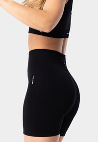 Black athletic shorts made of stretchy fabric, featuring a high waistband, smooth texture, and side logo detail.