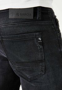 Vaqueros de mezclilla negra con un diseño elegante, con una etiqueta de cuero en la cintura y una pequeña etiqueta de logo en el bolsillo trasero.