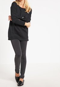 Felpa nera con scollatura rotonda, maniche lunghe e decorazione con stella sul davanti. Abbinata a jeans slim-fit grigio scuro e mocassini neri.