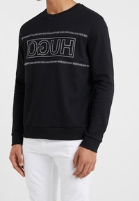Schwarzer Sweatshirt mit langen Ärmeln, gerippten Bündchen und Saum. Verfügt über ein weißes "HUGO"-Logo entlang der Brust. Hergestellt aus weichem Stoff.