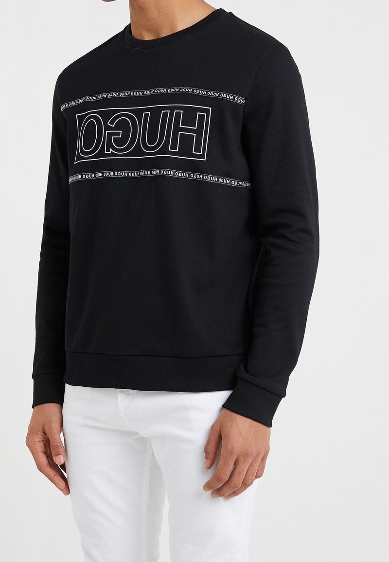 Schwarzer Sweatshirt mit langen Ärmeln, gerippten Bündchen und Saum. Verfügt über ein weißes "HUGO"-Logo entlang der Brust. Hergestellt aus weichem Stoff.