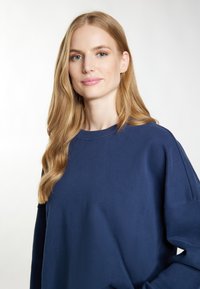 Granatowy sweatshirt z okrągłym dekoltem i długimi rękawami, o luźnym kroju i miękkiej teksturze. Minimalistyczny design, bez wzorów.