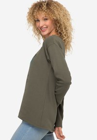 Olivegrünes Langarmshirt mit entspannter Passform, featuring einem grafischen Druck, Rundhalsausschnitt und glattem Baumwollstoff. Lässiger Stil.