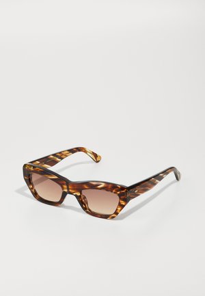 Lunettes de soleil en écaille de tortue avec une monture carrée épaisse, des verres dégradés et des branches élégantes présentant un motif subtil et un détail de logo.