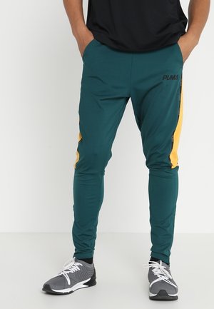 Teal athletic pants with yellow side stripes and a black logo. Made from stretchy material, designed for comfort and movement.