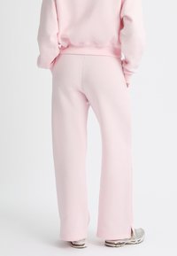 Roze sweatpants van een zachte stof, met een ontspannen pasvorm, uitlopende pijpen en zijspleten aan de zoom. Gecombineerd met grijze sneakers.