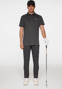 Grå pikétröja med krage och logotyp, kombinerad med matchande grå byxor. Vit golfhandske och skor kompletterar outfiten.