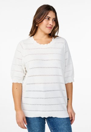 White knitted top with scalloped neckline and puff sleeves. Features horizontal stripes with openwork patterns. Paired with blue jeans.