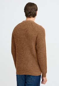 Brun strikket sweater med et struktureret mønster, rund halsudskæring og ribbede manchetter. Båret med blå jeans, set fra ryggen.