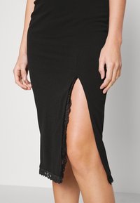 Černé upnuté šaty s bočním rozparkem, které mají na lemu detail z jemné černé krajky. Hladká textura látky, přiléhavý design.