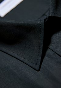 Schwarzer Stoff mit glatter Textur, mit einem umgeschlagenen Kragen und klaren Kanten. Sichtbare Nahtdetails entlang der Kanten.