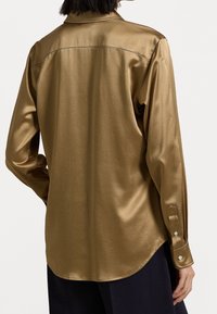 Långärmad skjorta i en metallisk guldnyans, tillverkad av slät satin. Har en knappad cuff och en rundad nederkant bak.