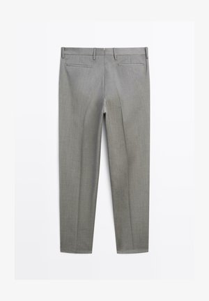 Grijze op maat gemaakte broek van gladde stof. Heeft een plooi aan de voorkant, twee achterzakken en een platte tailleband met riemlussen.