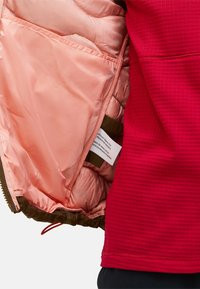 Rode geïsoleerde jas met een lichtroze voering en een binnenzak. Beschikt over een gestructureerde buitenstof en contrasterende ritsdetails.