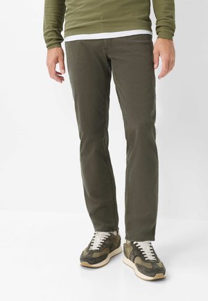 Uomo che indossa pantaloni casual verde oliva, sneakers verde oliva con lacci bianchi e un maglione verde oliva sopra una camicia bianca.