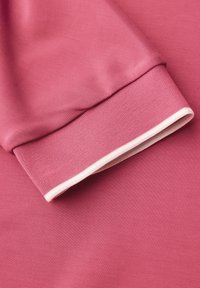 Tissu de sweat-shirt rose avec un poignet replié arborant une bordure blanche. Texture douce avec une finition lisse et des accents côtelés au niveau des manches.