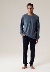 Niebieska koszula z długim rękawem uszyta z miękkiego materiału, w połączeniu z ciemnonawym spodniami na sznurek. Prosty design bez widocznych wzorów.