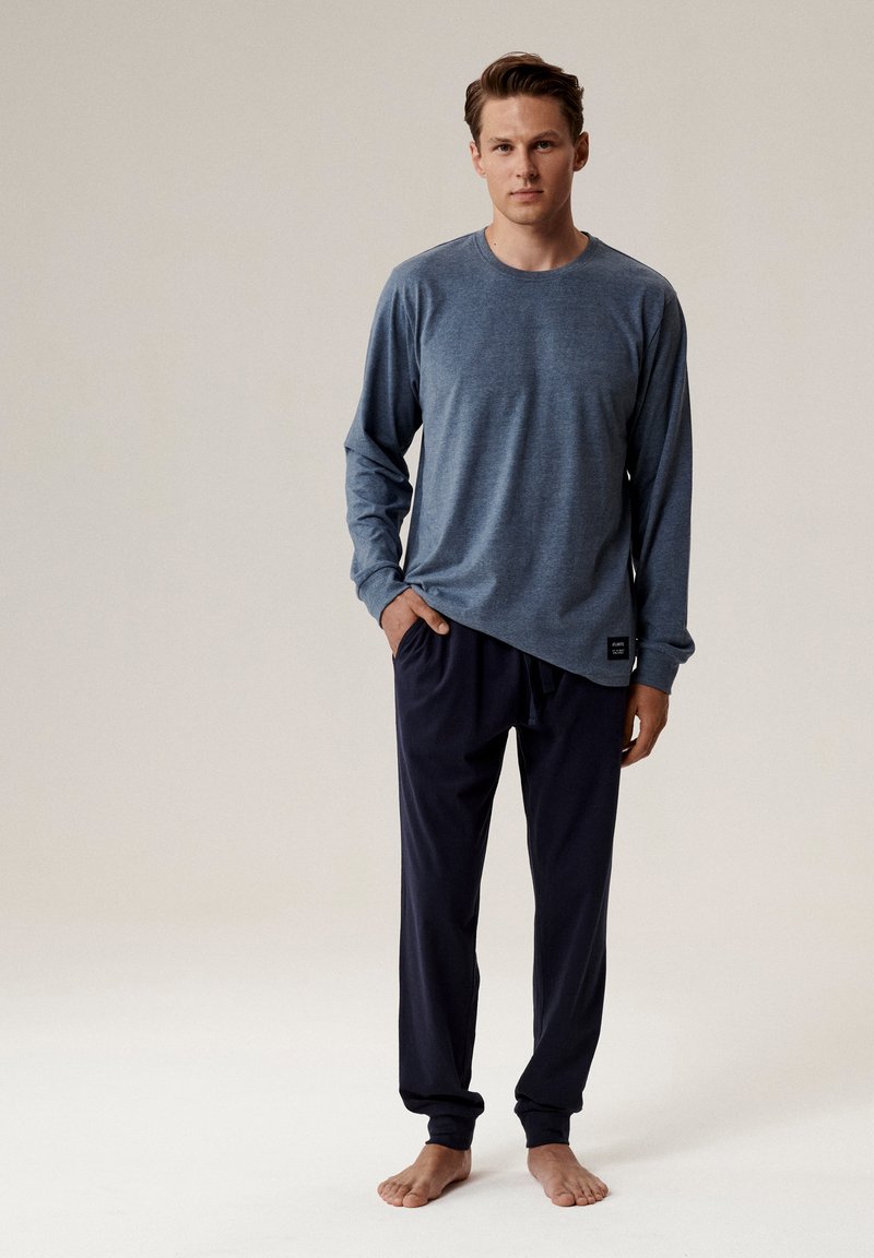 Niebieska koszula z długim rękawem uszyta z miękkiego materiału, w połączeniu z ciemnonawym spodniami na sznurek. Prosty design bez widocznych wzorów.