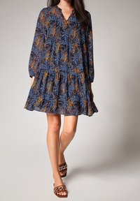 Robe bleue à motif floral avec manches longues, col en V, ourlet à volants et sandales marron ornées d'un accent chaîne. Tissu doux et fluide.