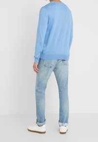 Ljusblå långärmad tröja med rundad halsringning, parat med blekta blå jeans och vita sneakers med bruna sulor.