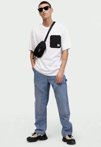 T-shirt branca de manga curta com bolso preto, jeans de corte largo azul claro, bolsa preta de ombro e óculos de sol pretos. Ténis com detalhes claros.