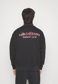 Schwarzer Sweatshirt mit lockerer Passform, auf der Rückseite mit einem roten und weißen Textgrafik, die "Carlo Gucci Milano 1978" liest.
