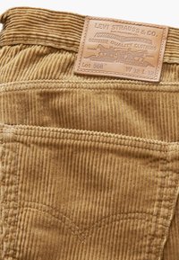 Pantalones de pana Levi Strauss en beige, con costuras verticales, una etiqueta de cuero con texto grabado y costuras clásicas en el bolsillo trasero.