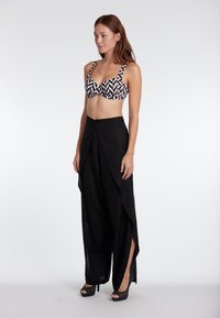 Black high-waisted pants with a draped design and side slits, paired with a geometric-patterned bra top in black and white.