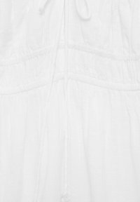 White dress featuring gathered elastic waistband, drawstring, and button detail. Fabric appears lightweight and slightly textured.
