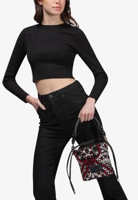 Top nero a maniche lunghe e corte abbinato a jeans neri a vita alta. Una borsa decorata con motivi rossi e bianchi su una base nera, caratterizzata da un manico intrecciato.