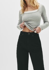 Haut à manches longues en rib avec un col carré de couleur gris clair, associé à un jean noir taille haute avec fermeture à bouton et poches.