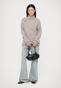 Pull en maille côtelée gris avec des écussons en forme de cœur sur les manches. Associé à un jean clair évasé et un petit sac à main noir.