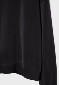 Felpa nera con texture morbida, polsini e orlo a coste. Il design presenta una vestibilità comoda e uno stile minimalista.