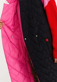 Kamizelka pikowana z czarnym wierzchem w serca i jasnoróżowym wnętrzem. Posiada zatrzaski oraz kontrastowe wykończenie krawędzi.