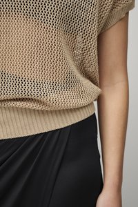 Beige open-knit trui met korte mouwen en een geribbelde zoom, gecombineerd met een zwarte stoffen rok. Heeft een losse fit en een gestructureerd ontwerp.