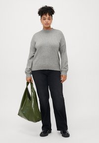 Siv sweater z ribanim ovratnikom, v kombinaciji s črnimi kavbojkami. Nosila ima sijočo zeleno torbico in črne škornje. Struktura pletenine.