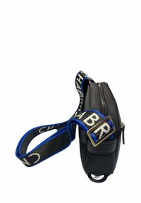 Bolso cruzado negro con una textura suave, que cuenta con un cierre de cremallera y una correa estampada en negro y azul con letras en negrita.