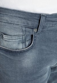 Jeans de mezclilla azul oscuro con un lavado desgastado, que presentan un bolsillo delantero, cierre de botón y costuras visibles a lo largo de la cinturilla y las costuras.