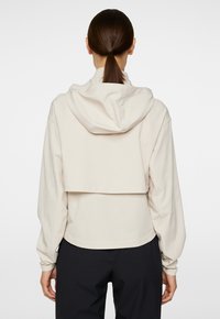 Korte lichtbeige sweatshirt met een capuchon, met een losse pasvorm en lange mouwen. Soepele stof met een eenvoudig ontwerp en minimale details.
