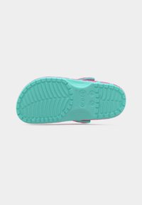 Σόλα ενός παπουτσιού Crocs σε τιρκουάζ και ροζ χρώμα με υφασμένο πέλμα και ενδείξεις μεγέθους σε λευκό φόντο.