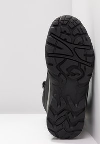 Semelle de chaussure de sport noire avec un design texturé et robuste, dotée de profonds rainures pour une traction et une stabilité accrues ; panneaux latéraux lisses visibles.