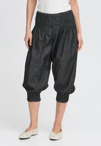 Pantalons en denim foncé, coupés, avec une taille smockée et des poignets, présentant une silhouette ample et flottante ainsi qu'une texture lisse.
