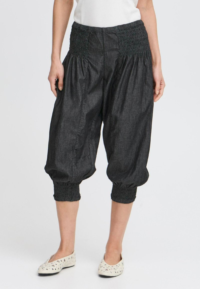 Pantalons en denim foncé, coupés, avec une taille smockée et des poignets, présentant une silhouette ample et flottante ainsi qu'une texture lisse.