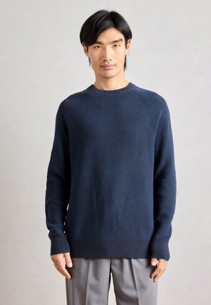 Mornarica rebrasti pleteni pulover s okruglim izrezom, dugim rukavima i kontrastnim manžetama. Ima opušteni kroj i teksturirani materijal.