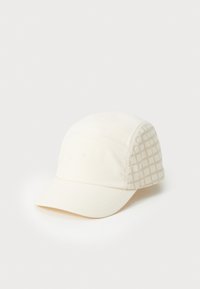 Vit keps gjord av texturerad tyg med en platt skärm. Ena sidan har ett subtilt geometriskt mönster i ljusbeige.