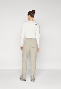 Hvit langermet skjorte med en kortet design, kombinert med lyse beige bukser. Skjorten har en svart logo på baksiden.