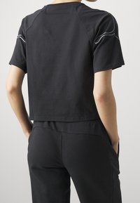 Camiseta negra de manga corta con un diseño recortado. Presenta una sutileza de costura gris a lo largo de los hombros. Tejido suave con una textura lisa.