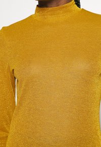 Hochgeschlossener, langärmliger Top in Goldglitter, aus einem strukturierten Stoff gefertigt, mit einer taillierten Passform und subtilen Schimmer-Effekten.